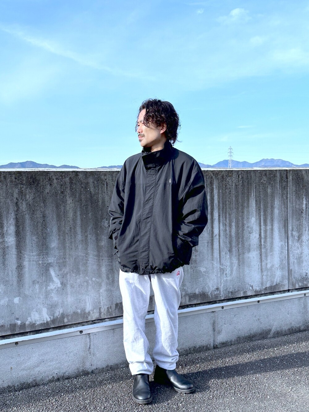 ブラック系のナイロンジャケット、グレー系のスウェットパンツ、ブラック系のブーツを着用したメンズの春コーディネートの2枚目の写真