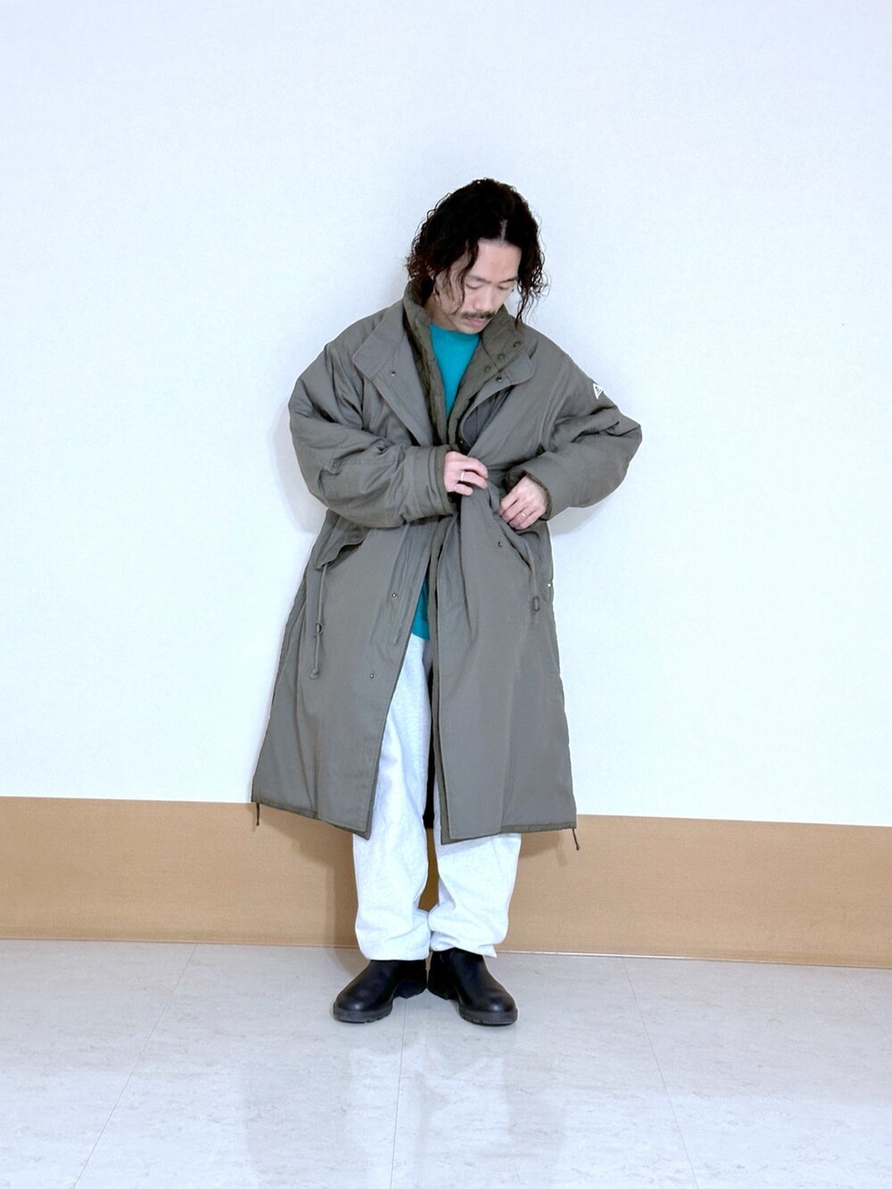 グリーン系のモッズコート、グレー系のスウェットパンツ、ブラック系のブーツを着用したメンズの冬コーディネートの2枚目の写真