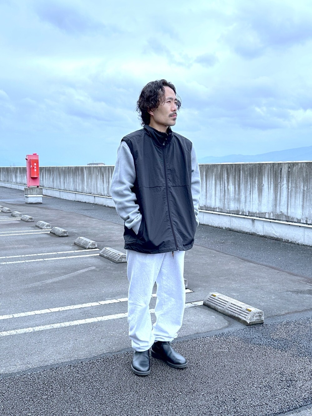 ブラック系のベスト、グレー系のニット/セーター、グレー系のスウェットパンツを着用したメンズの春コーディネートの2枚目の写真