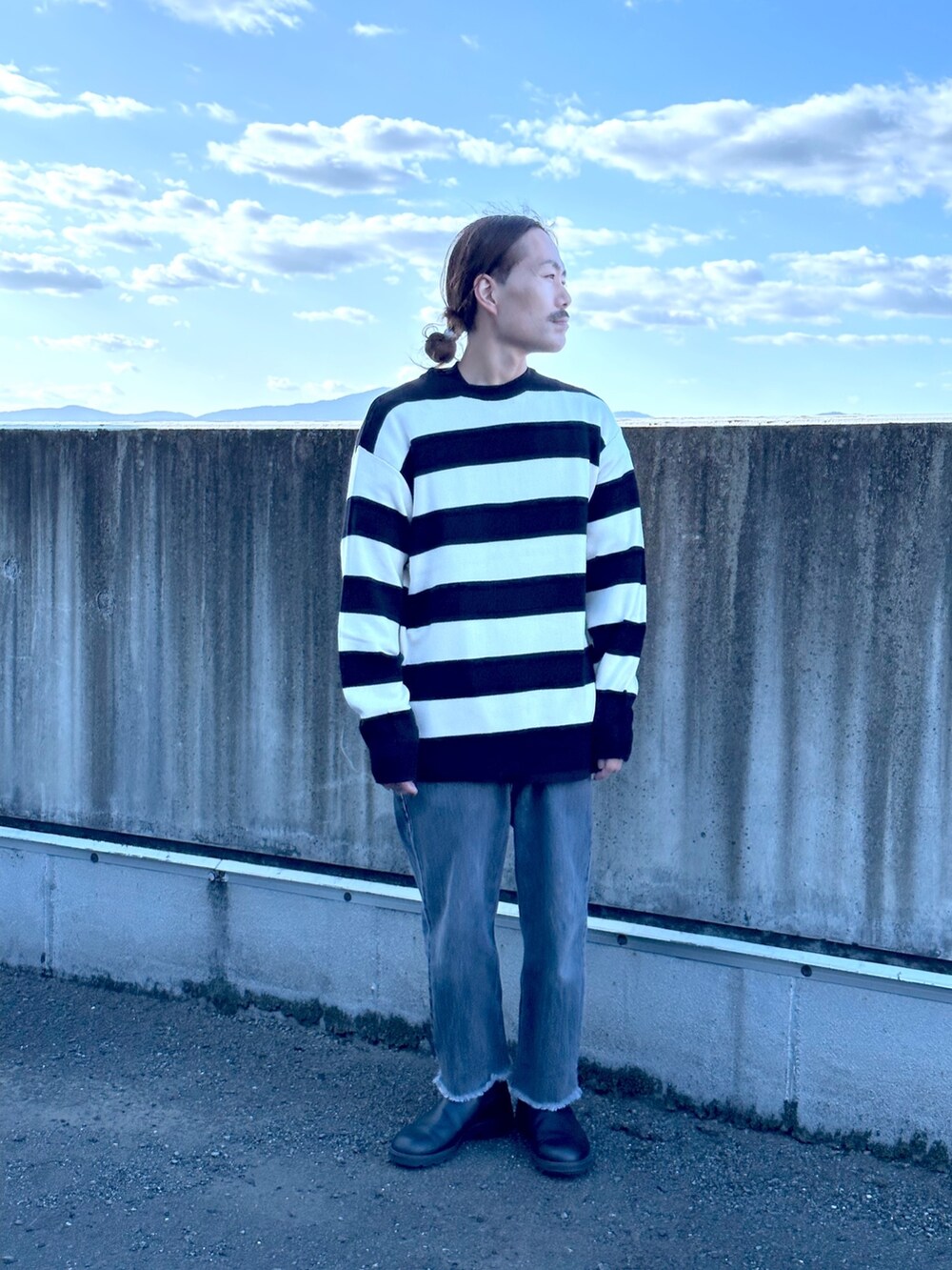 ブラック系のニット/セーター、ブルー系のデニムパンツ、ブラック系のブーツを着用したメンズの秋コーディネートの2枚目の写真