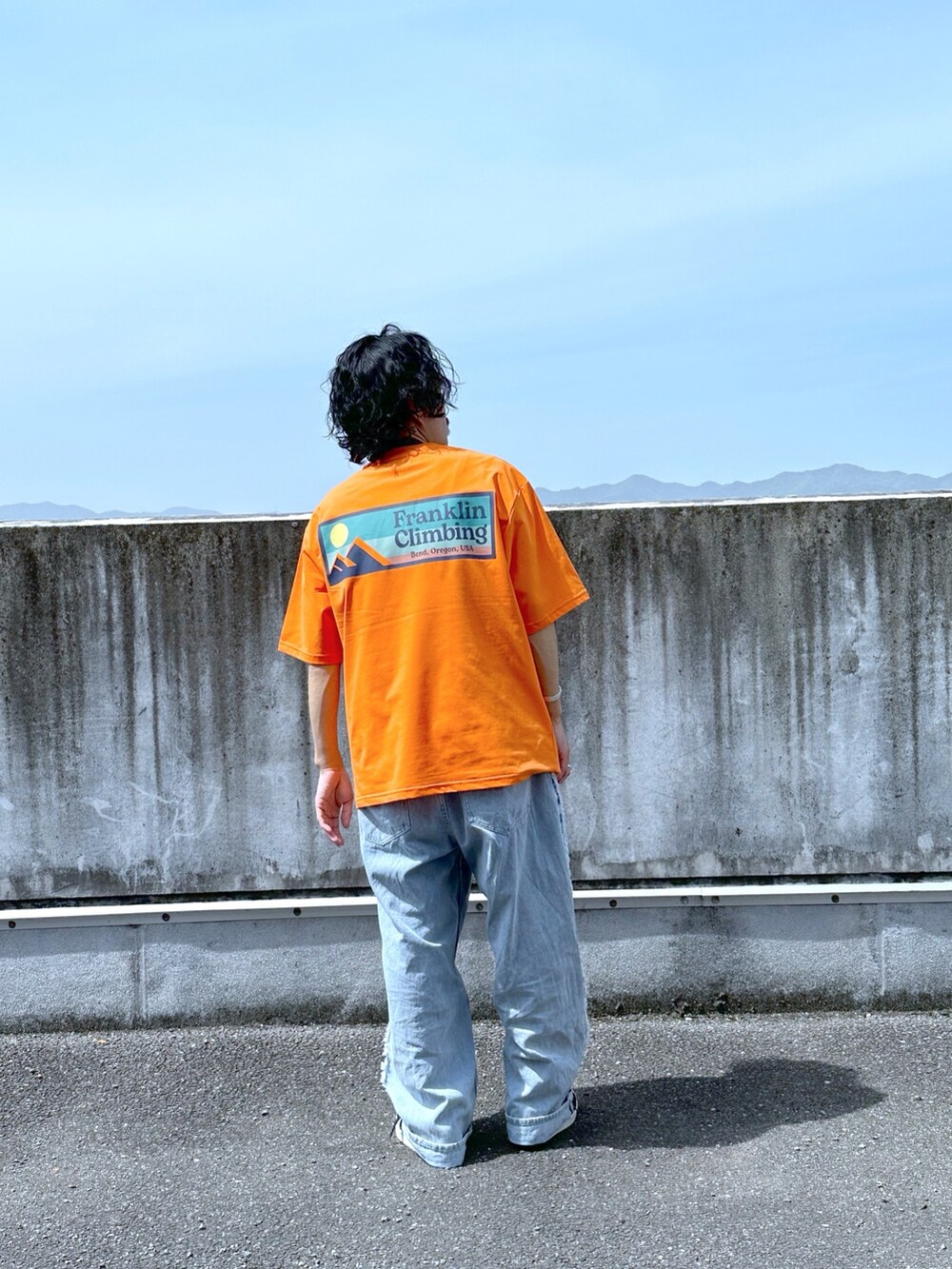 オレンジ系のTシャツ/カットソー、ブルー系のデニムパンツを着用したメンズの春コーディネートの2枚目の写真