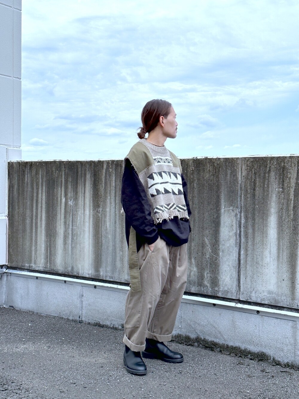 グリーン系のベスト、グリーン系のチノパンツ、ブラック系のブーツを着用したメンズの秋コーディネートの2枚目の写真