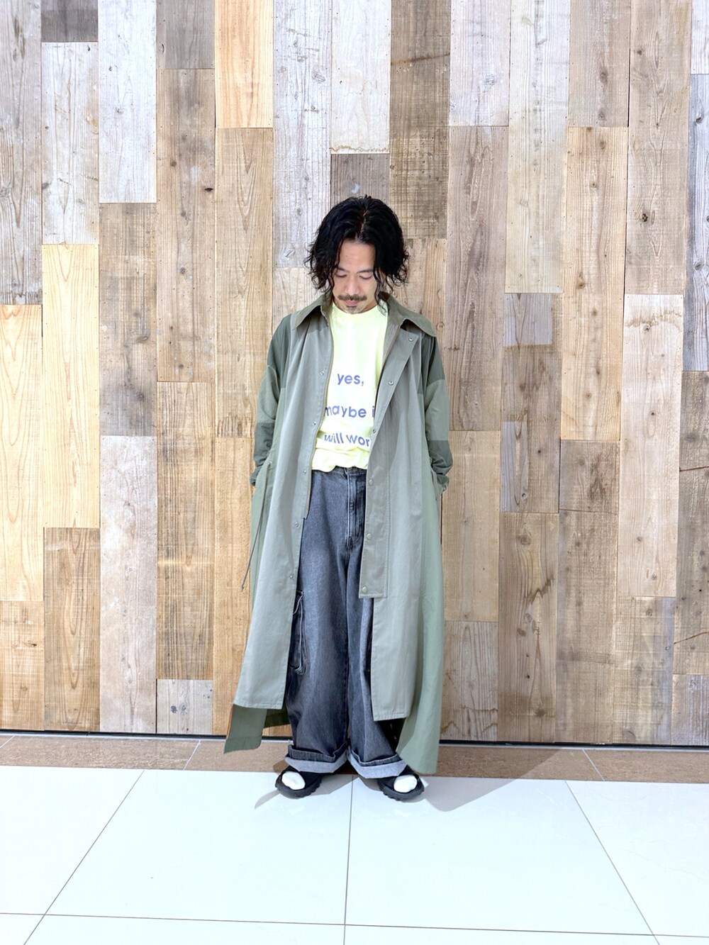 グリーン系のステンカラーコート、イエロー系のTシャツ/カットソー、ブラック系のカーゴパンツを着用したメンズの秋コーディネートの2枚目の写真