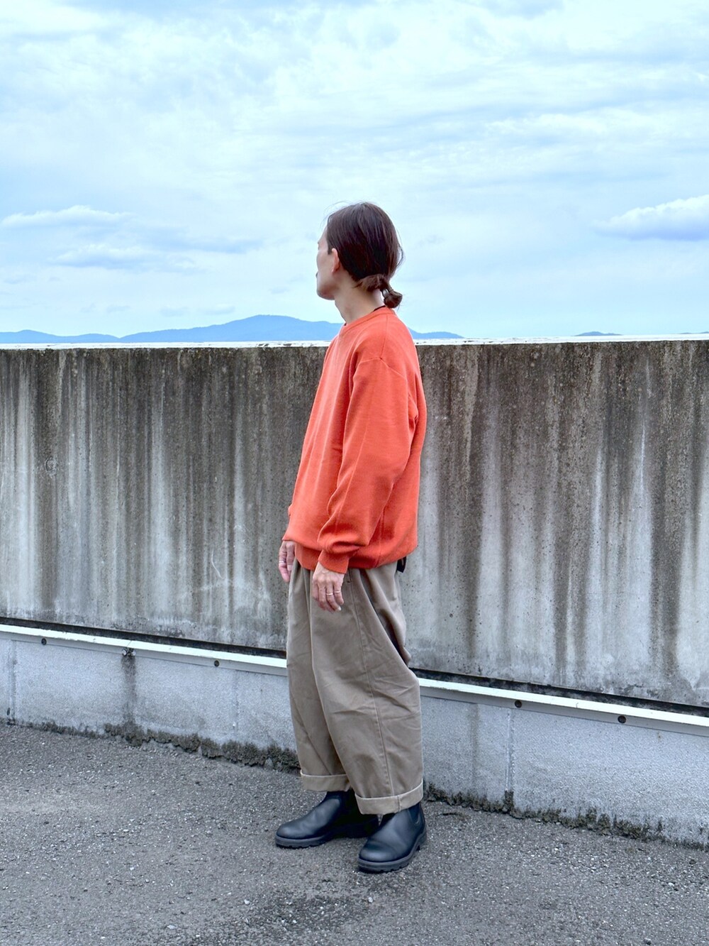 オレンジ系のニット/セーター、グリーン系のチノパンツ、ブラック系のブーツを着用したメンズの秋コーディネートの2枚目の写真