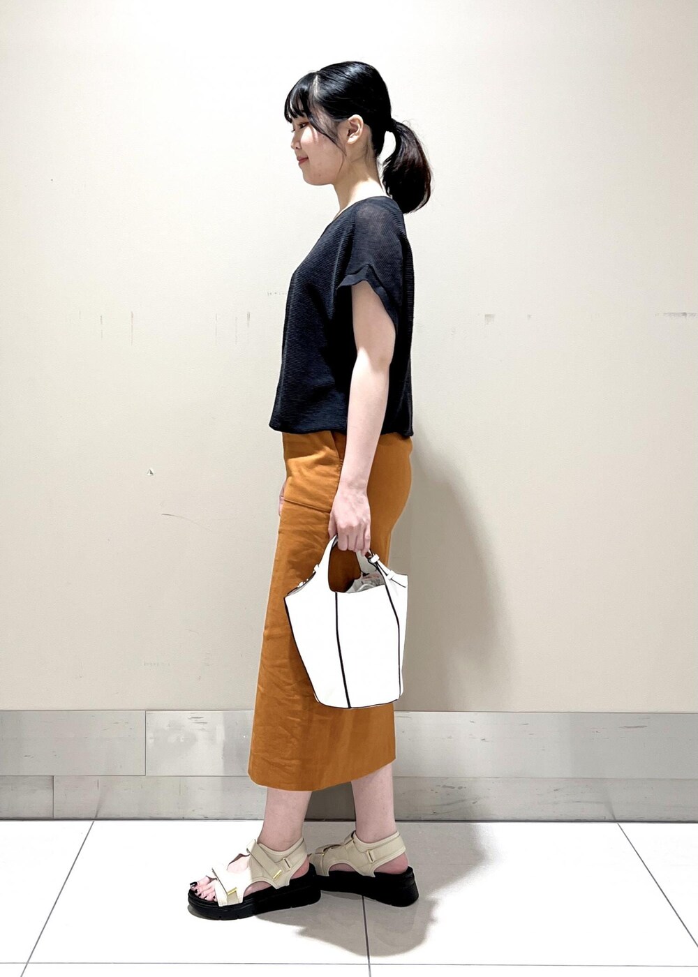 ホワイト系のハンドバッグ、ホワイト系のサンダル、オレンジ系のスカートを着用したレディースの夏コーディネートの2枚目の写真