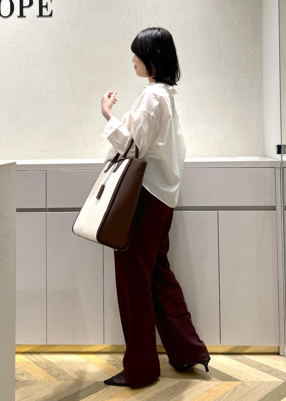 ブラウン系のトートバッグ、ホワイト系のシャツ/ブラウス、ブラック系のパンプスを着用したレディースの春コーディネートの2枚目の写真