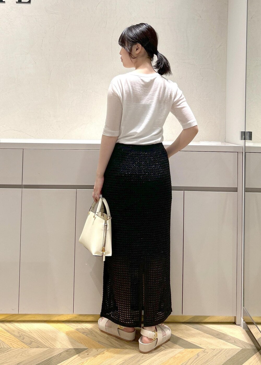 ホワイト系のハンドバッグ、ベージュ系のサンダル、ホワイト系のTシャツ/カットソーを着用したレディースの夏コーディネートの3枚目の写真