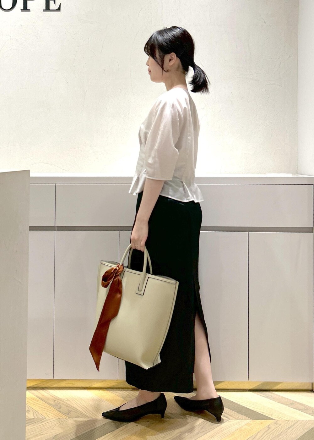 ブラック系のパンプス、ベージュ系のトートバッグ、ブラック系のスカートを着用したレディースの夏コーディネートの2枚目の写真