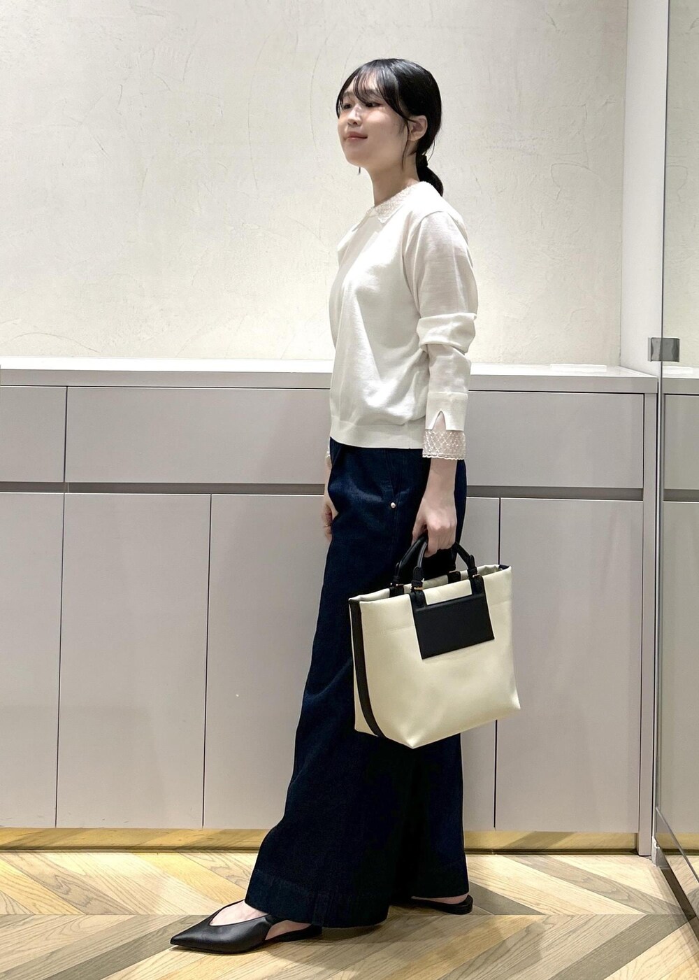 ブラック系のパンプス、ホワイト系のトートバッグ、ブルー系のデニムパンツを着用したレディースの冬コーディネートの2枚目の写真