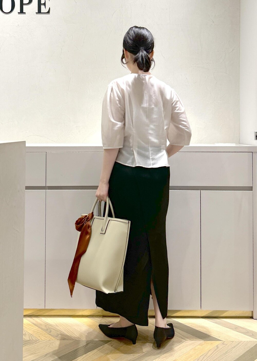 ブラック系のパンプス、ベージュ系のトートバッグ、ブラック系のスカートを着用したレディースの夏コーディネートの3枚目の写真