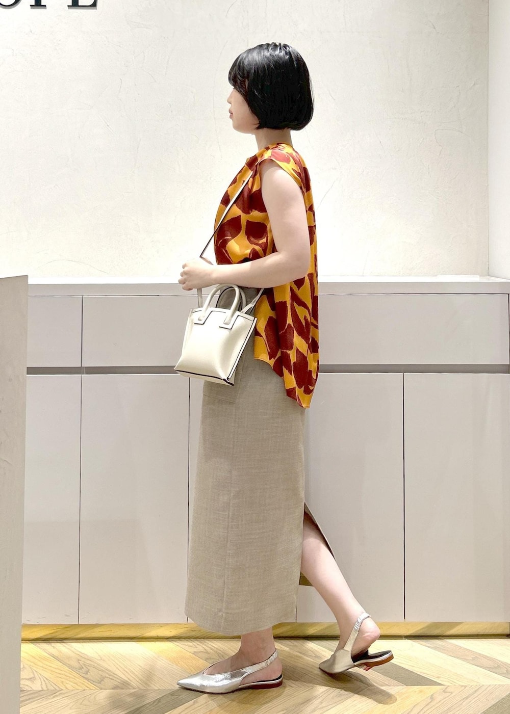 シルバー系のパンプス、ベージュ系のスカート、オレンジ系のシャツ/ブラウスを着用したレディースの夏コーディネートの2枚目の写真