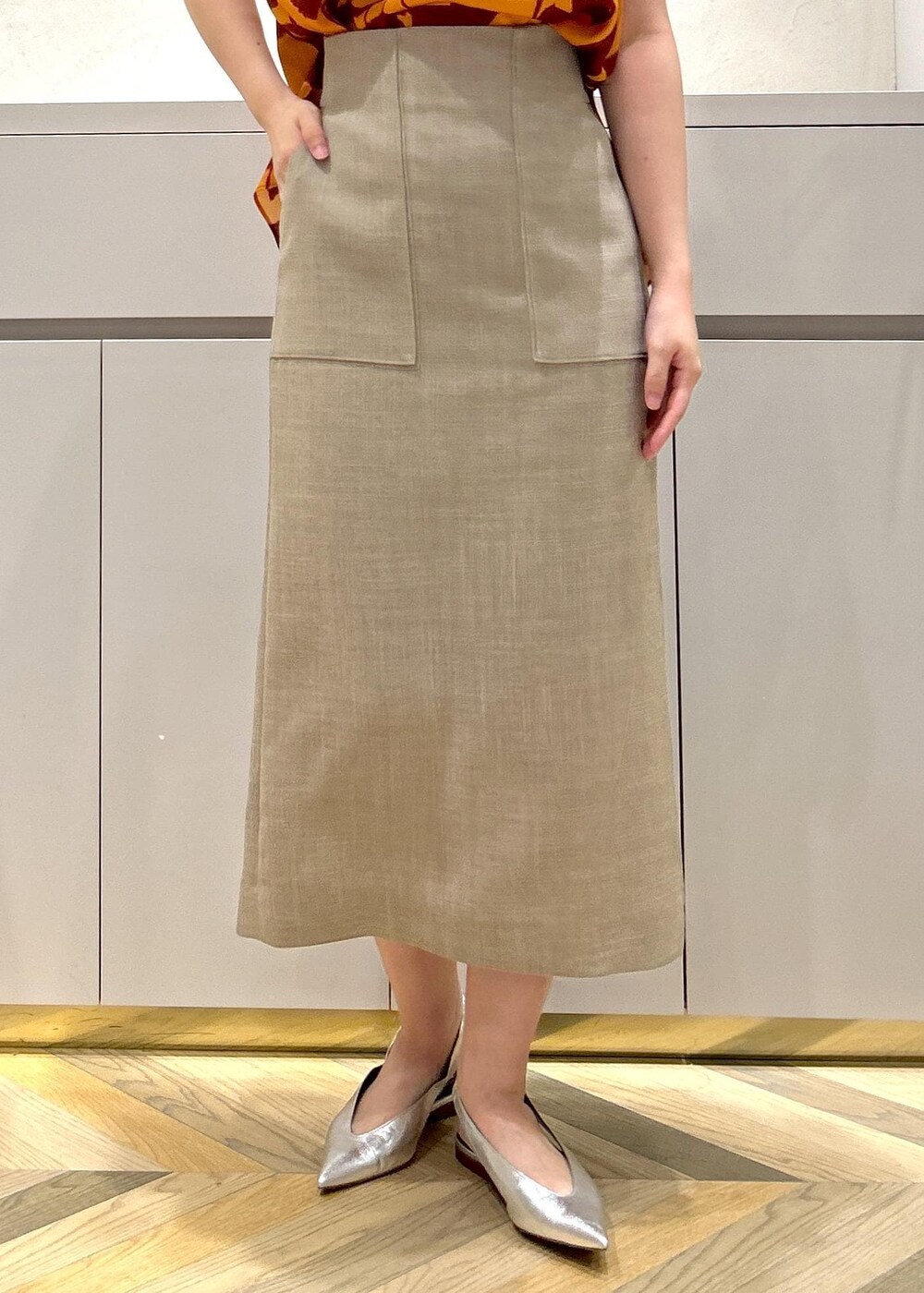 シルバー系のパンプス、ベージュ系のスカート、オレンジ系のシャツ/ブラウスを着用したレディースの夏コーディネートの7枚目の写真