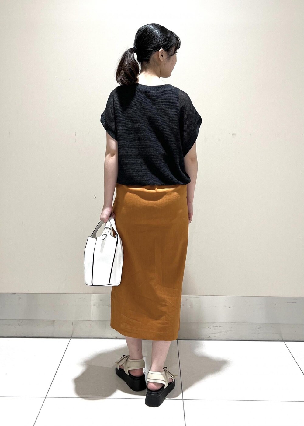 ホワイト系のハンドバッグ、ホワイト系のサンダル、オレンジ系のスカートを着用したレディースの夏コーディネートの3枚目の写真