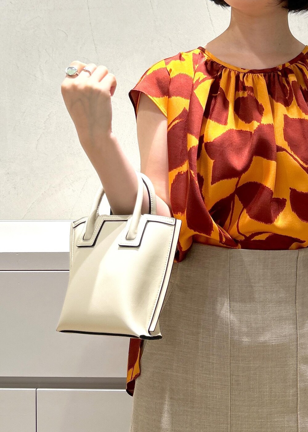 シルバー系のパンプス、ベージュ系のスカート、オレンジ系のシャツ/ブラウスを着用したレディースの夏コーディネートの9枚目の写真