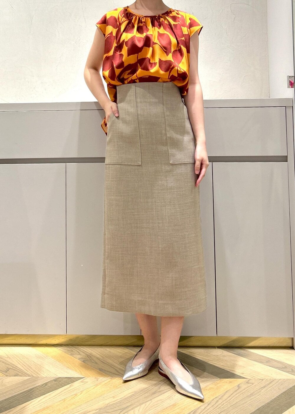 シルバー系のパンプス、ベージュ系のスカート、オレンジ系のシャツ/ブラウスを着用したレディースの夏コーディネートの4枚目の写真