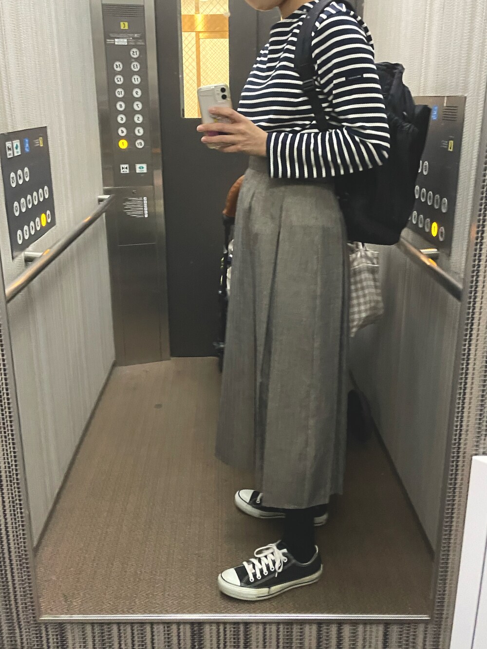 グレー系のスカート、ブラック系のトップス、ブラック系のスニーカーを着用したレディースの秋コーディネートの2枚目の写真