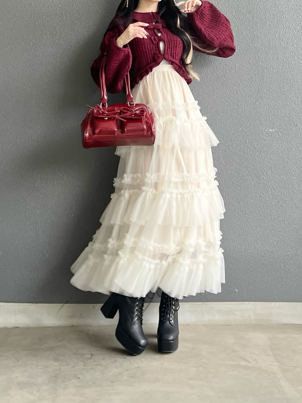 レッド系のバッグ、ホワイト系のスカート、ブラック系のブーツを着用したレディースの秋コーディネートの4枚目の写真