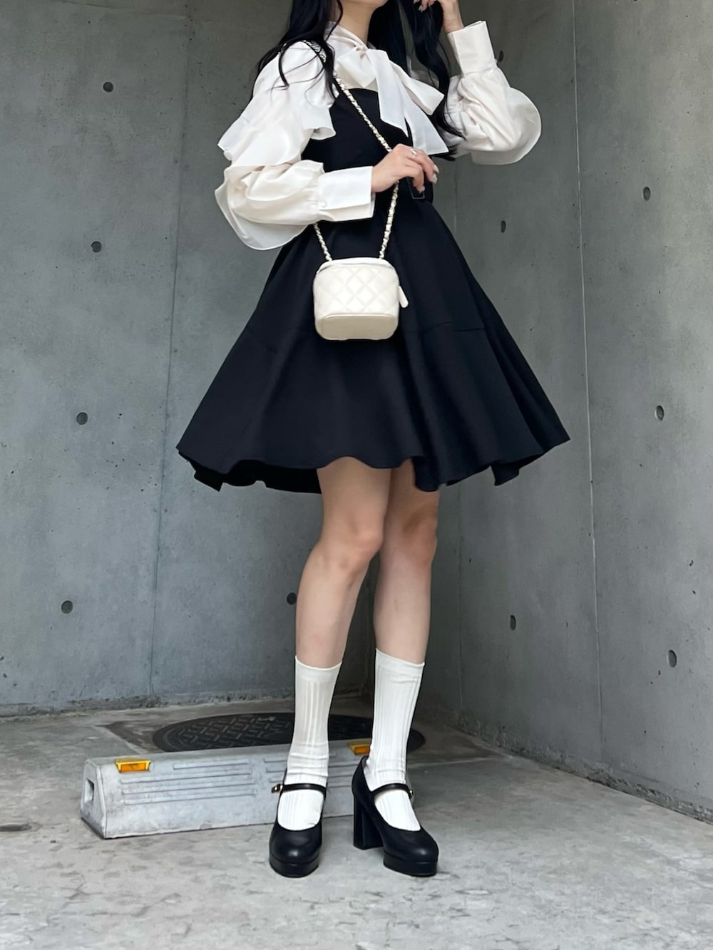 ホワイト系のバッグ、ブラック系のジャンパースカート、ブラック系のパンプスを着用したレディースの秋コーディネートの4枚目の写真