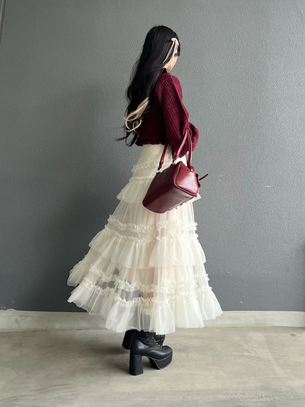 レッド系のバッグ、ホワイト系のスカート、ブラック系のブーツを着用したレディースの秋コーディネートの3枚目の写真