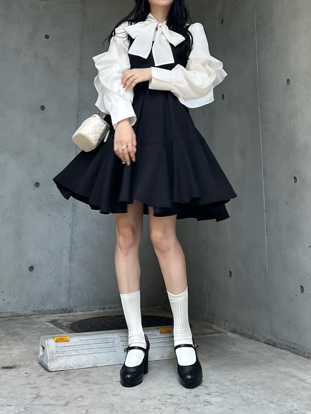 ホワイト系のバッグ、ブラック系のジャンパースカート、ブラック系のパンプスを着用したレディースの秋コーディネートの5枚目の写真