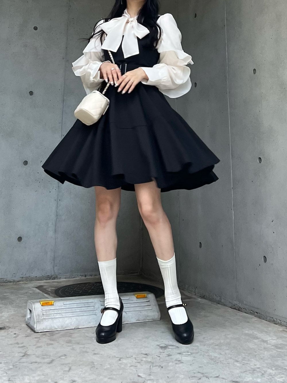 ホワイト系のバッグ、ブラック系のジャンパースカート、ブラック系のパンプスを着用したレディースの秋コーディネートの2枚目の写真