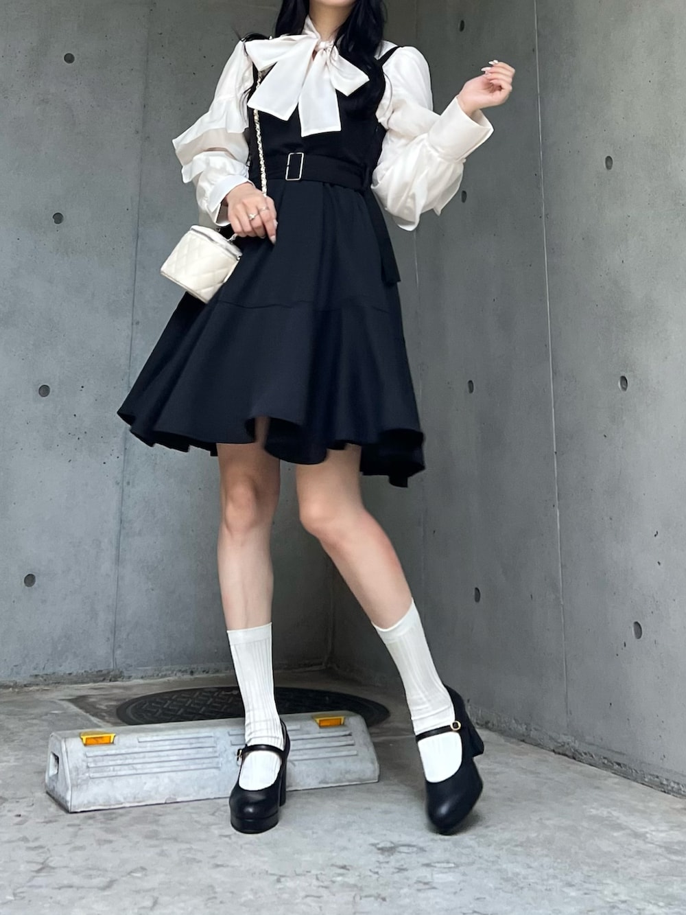 ホワイト系のバッグ、ブラック系のジャンパースカート、ブラック系のパンプスを着用したレディースの秋コーディネートの3枚目の写真