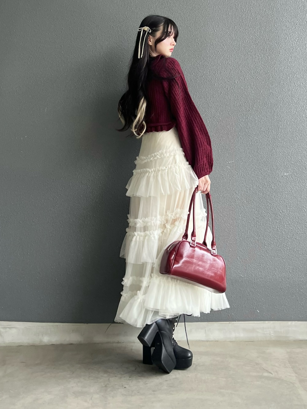 レッド系のバッグ、ホワイト系のスカート、ブラック系のブーツを着用したレディースの秋コーディネートの2枚目の写真