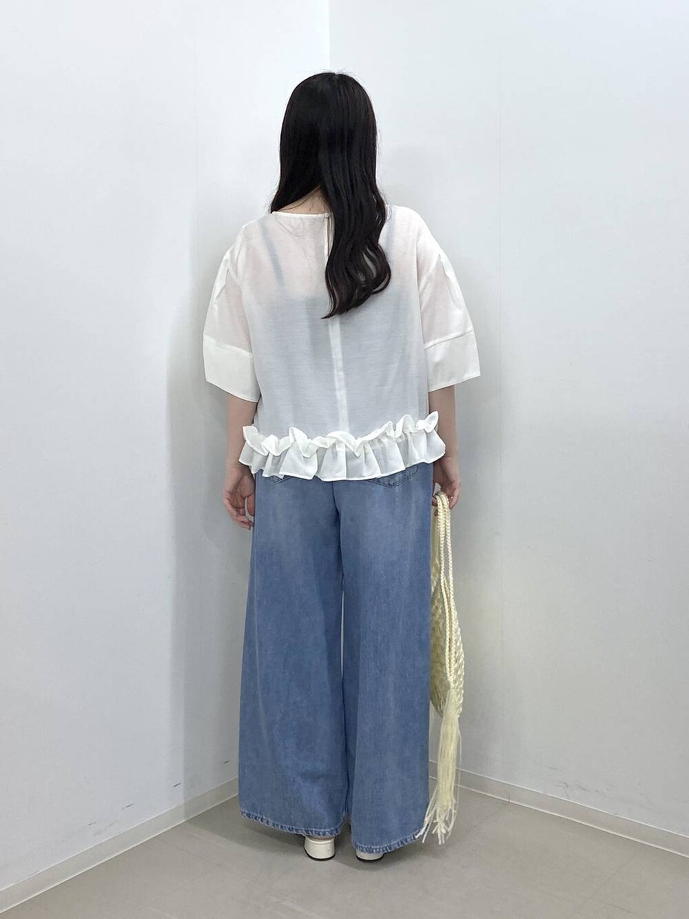 ホワイト系のハンドバッグ、ブルー系のデニムパンツ、ホワイト系のパンプスを着用したレディースの夏コーディネートの3枚目の写真