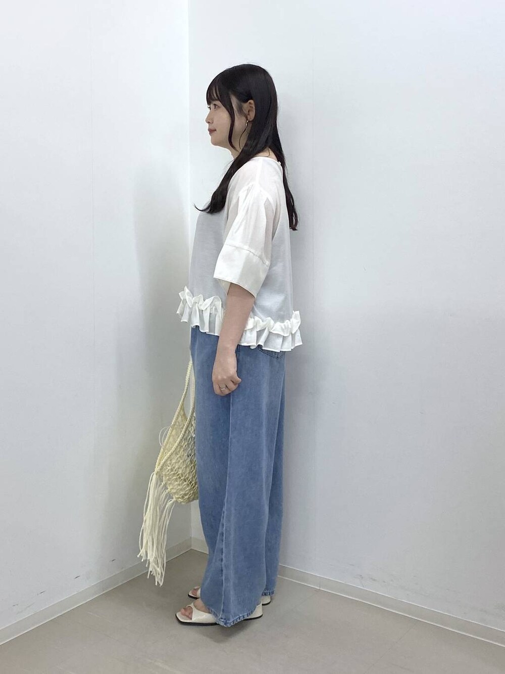ホワイト系のハンドバッグ、ブルー系のデニムパンツ、ホワイト系のパンプスを着用したレディースの夏コーディネートの2枚目の写真