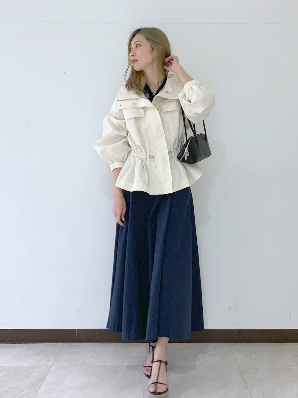 ブラック系のサンダル、ブラック系のハンドバッグ、ホワイト系のブルゾンを着用したレディースの春コーディネートの5枚目の写真