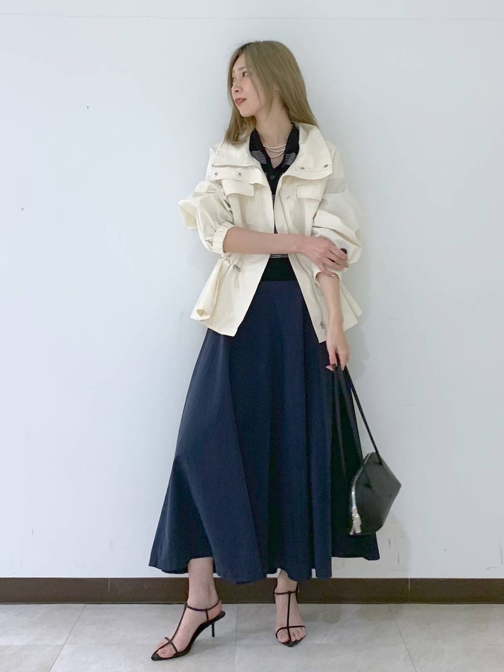 ブラック系のサンダル、ブラック系のハンドバッグ、ホワイト系のブルゾンを着用したレディースの春コーディネートの2枚目の写真