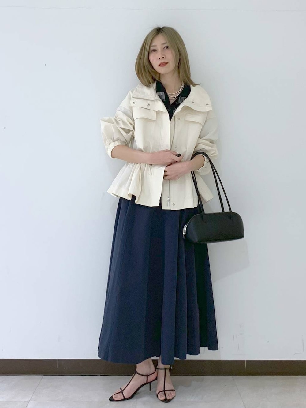 ブラック系のサンダル、ブラック系のハンドバッグ、ホワイト系のブルゾンを着用したレディースの春コーディネートの6枚目の写真