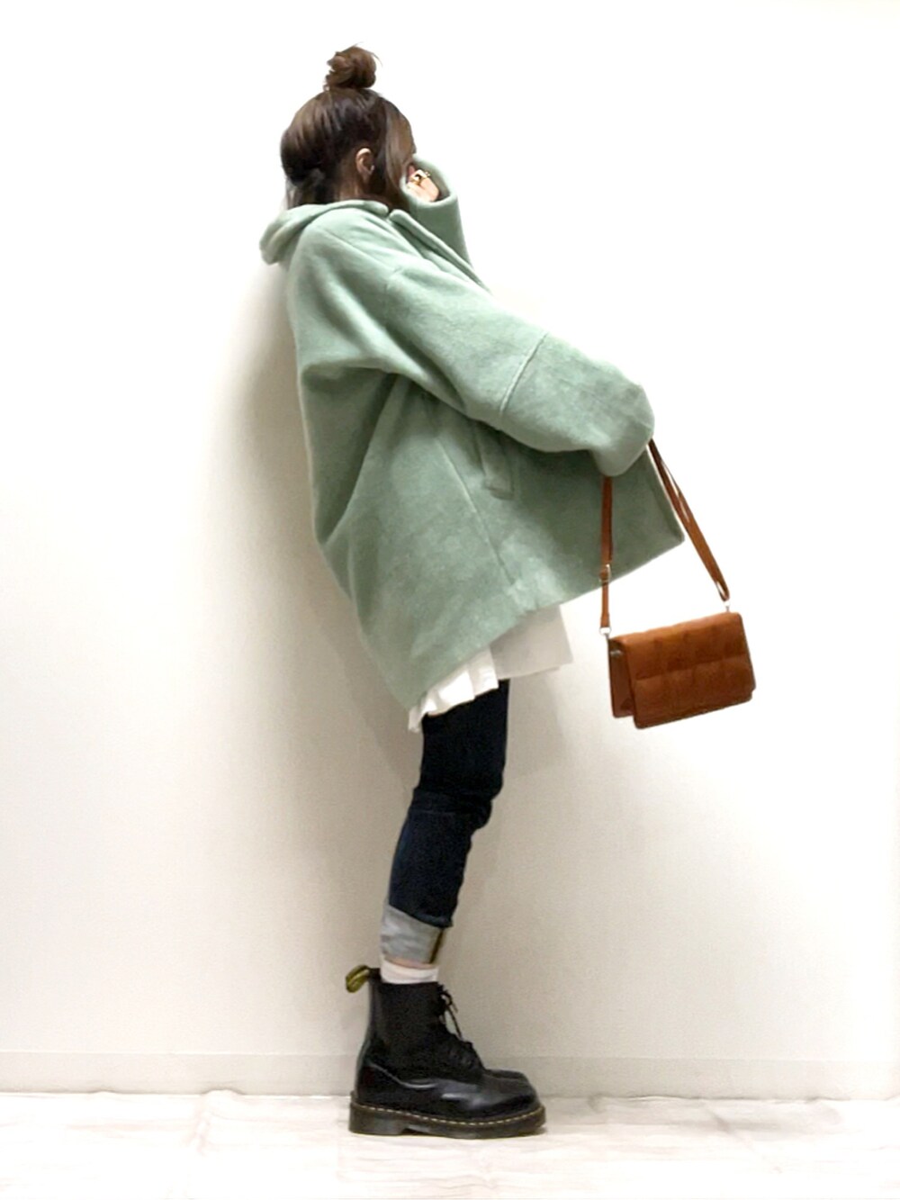 グリーン系のチェスターコート、ブラウン系のクラッチバッグ、ブラック系のブーツを着用したレディースの秋コーディネートの2枚目の写真