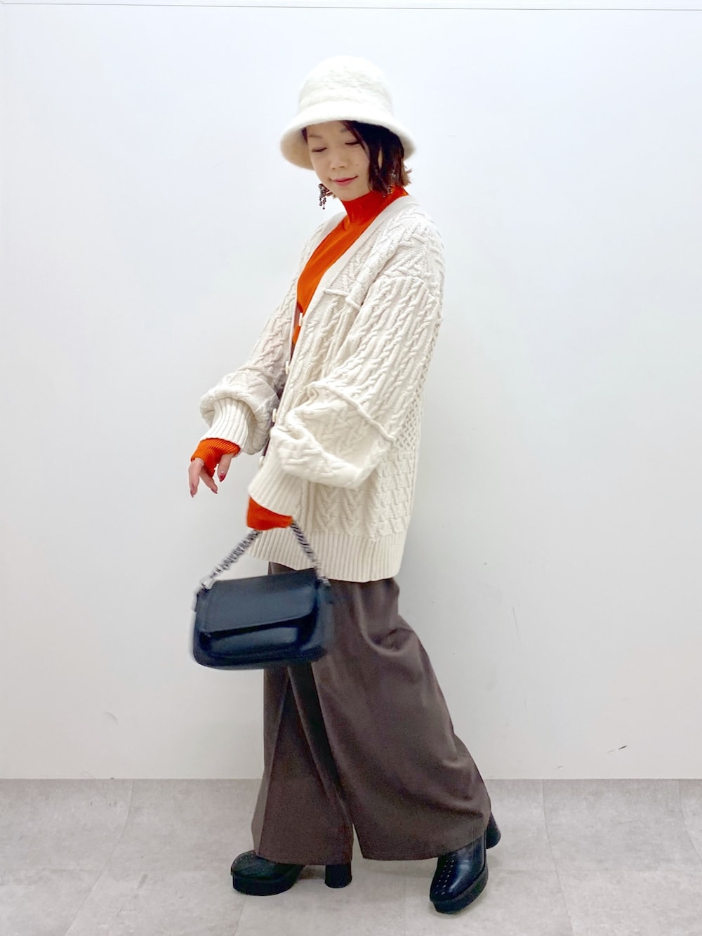 オレンジ系のトップス、ブラック系のバッグ、ブラック系のブーツを着用したレディースの秋コーディネートの2枚目の写真