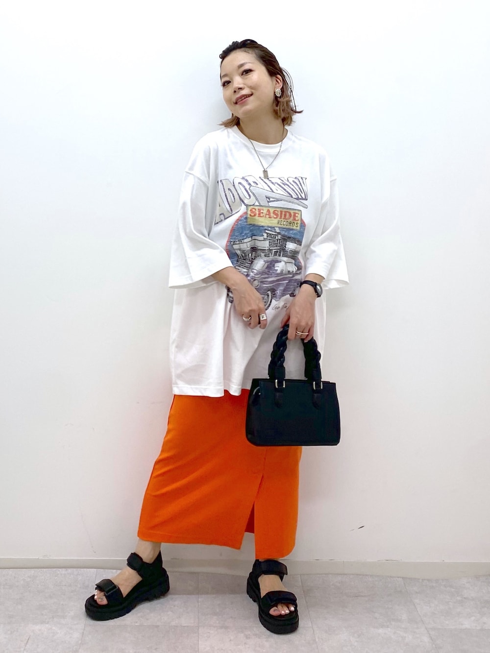 ホワイト系のTシャツ/カットソー、オレンジ系のスカート、ブラック系のショルダーバッグを着用したレディースの夏コーディネートの2枚目の写真