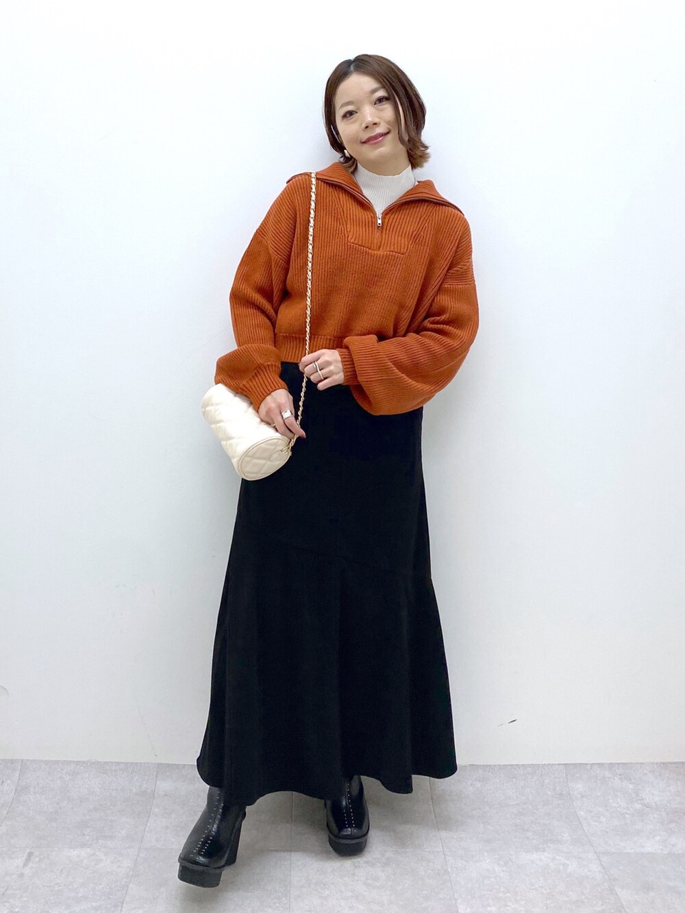 ブラック系のスカート、ホワイト系のバッグ、オレンジ系のニット/セーターを着用したレディースの秋コーディネートの5枚目の写真