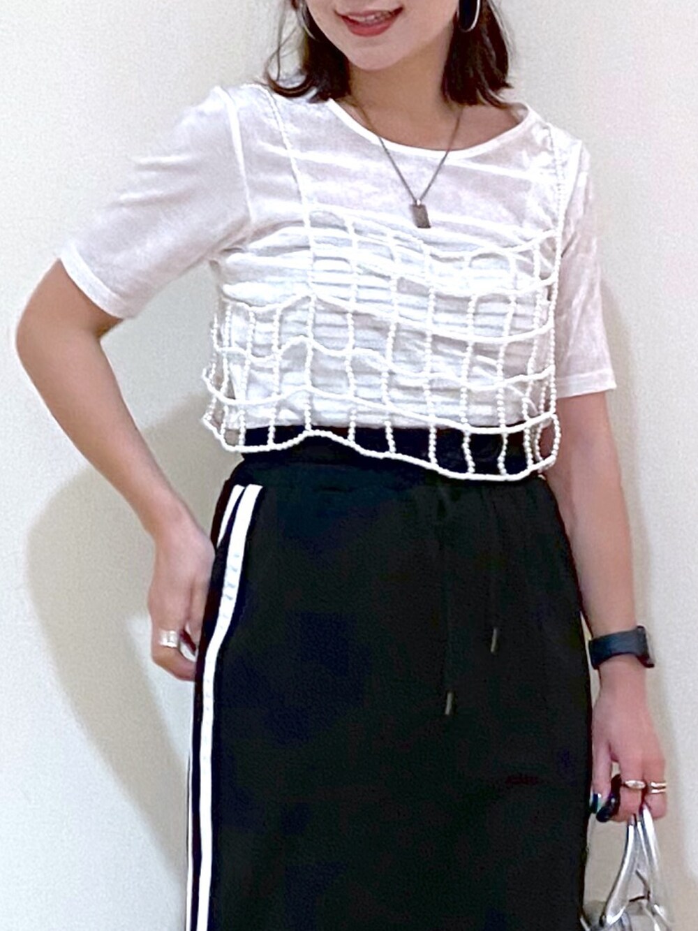 ブラック系のスカート、シルバー系のショルダーバッグ、ホワイト系のスニーカーを着用したレディースの夏コーディネートの2枚目の写真