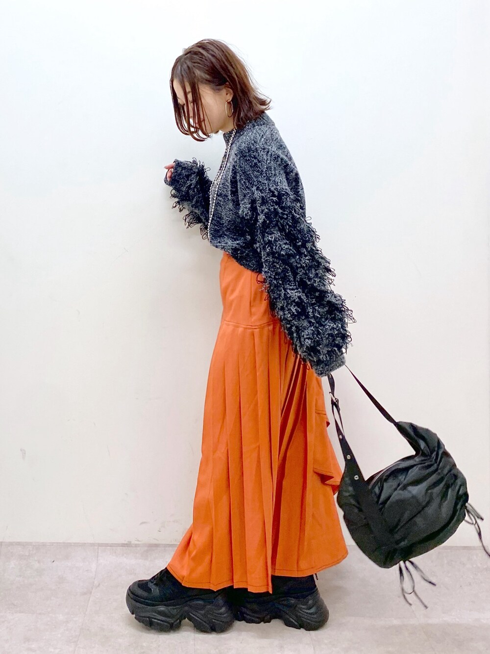 ブラック系のニット/セーター、オレンジ系のスカート、ブラック系のショルダーバッグを着用したレディースの冬コーディネートの5枚目の写真