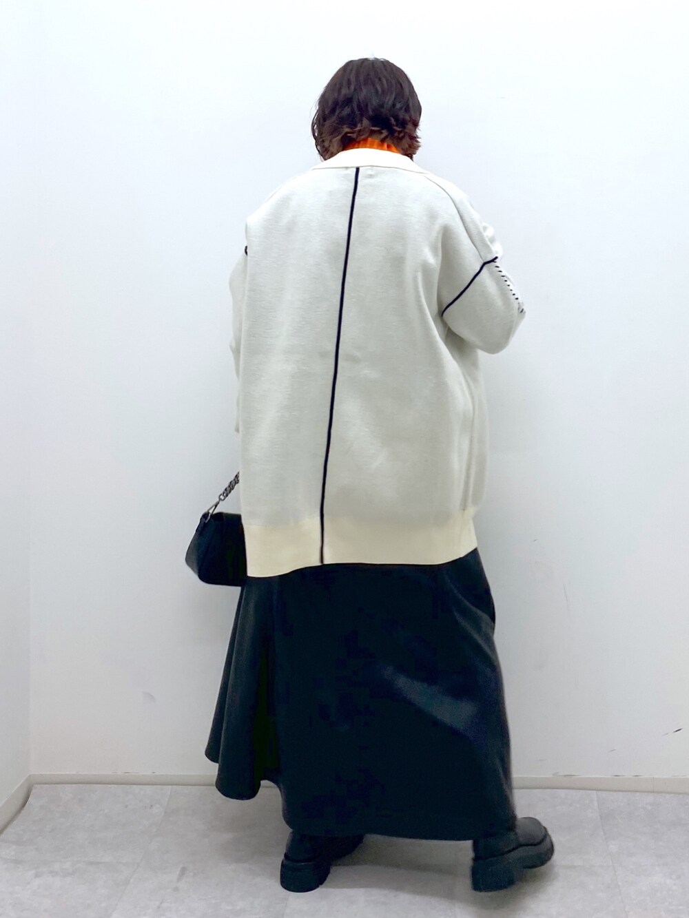 ブラック系のスカート、ブラック系のバッグ、オレンジ系のトップスを着用したレディースの秋コーディネートの4枚目の写真