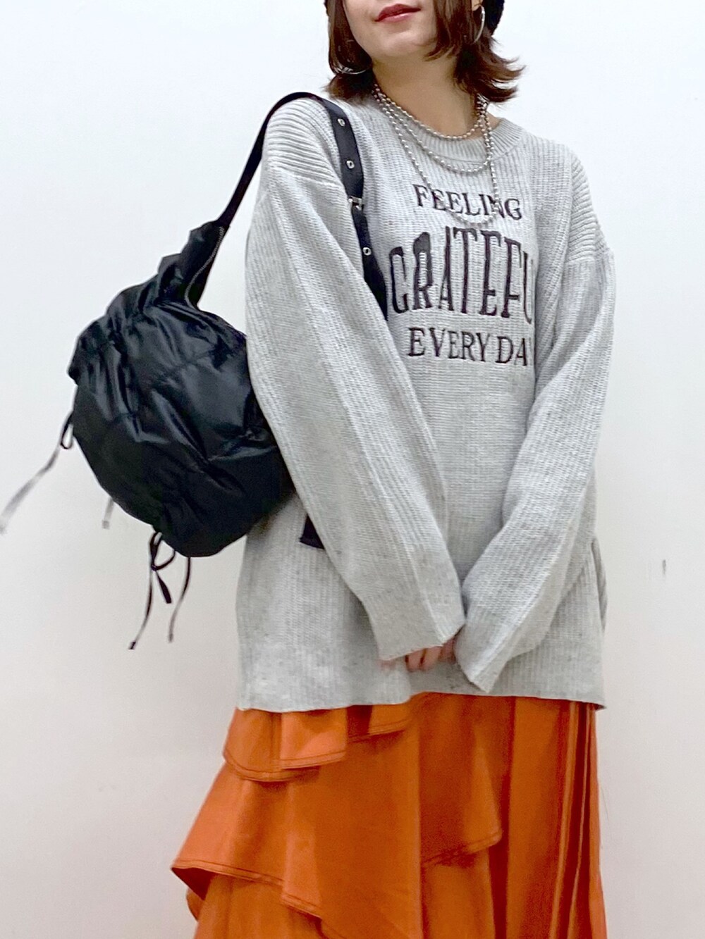 グレー系のニット/セーター、オレンジ系のスカート、ブラック系のローファーを着用したレディースの冬コーディネートの2枚目の写真