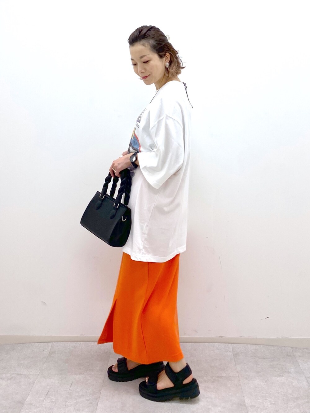 ホワイト系のTシャツ/カットソー、オレンジ系のスカート、ブラック系のショルダーバッグを着用したレディースの夏コーディネートの3枚目の写真