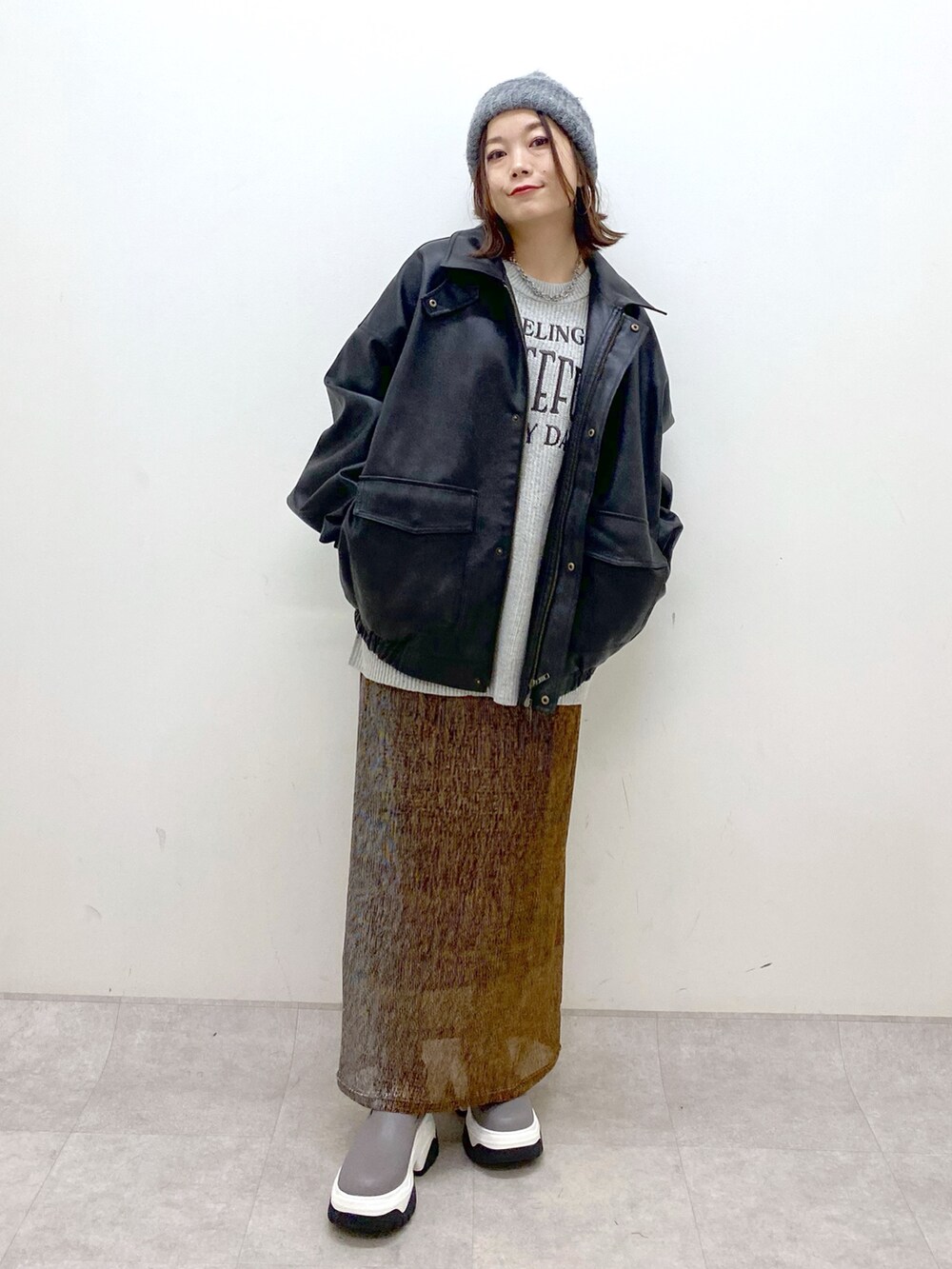 グレー系のニット/セーター、ブラック系のブルゾン、ゴールド系のスカートを着用したレディースの秋コーディネートの9枚目の写真