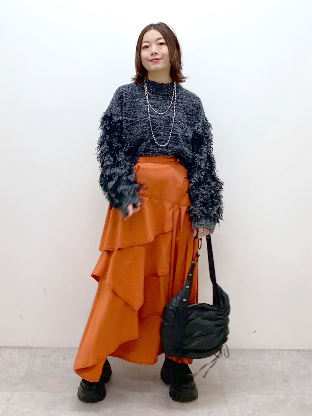 ブラック系のニット/セーター、オレンジ系のスカート、ブラック系のショルダーバッグを着用したレディースの冬コーディネートの8枚目の写真
