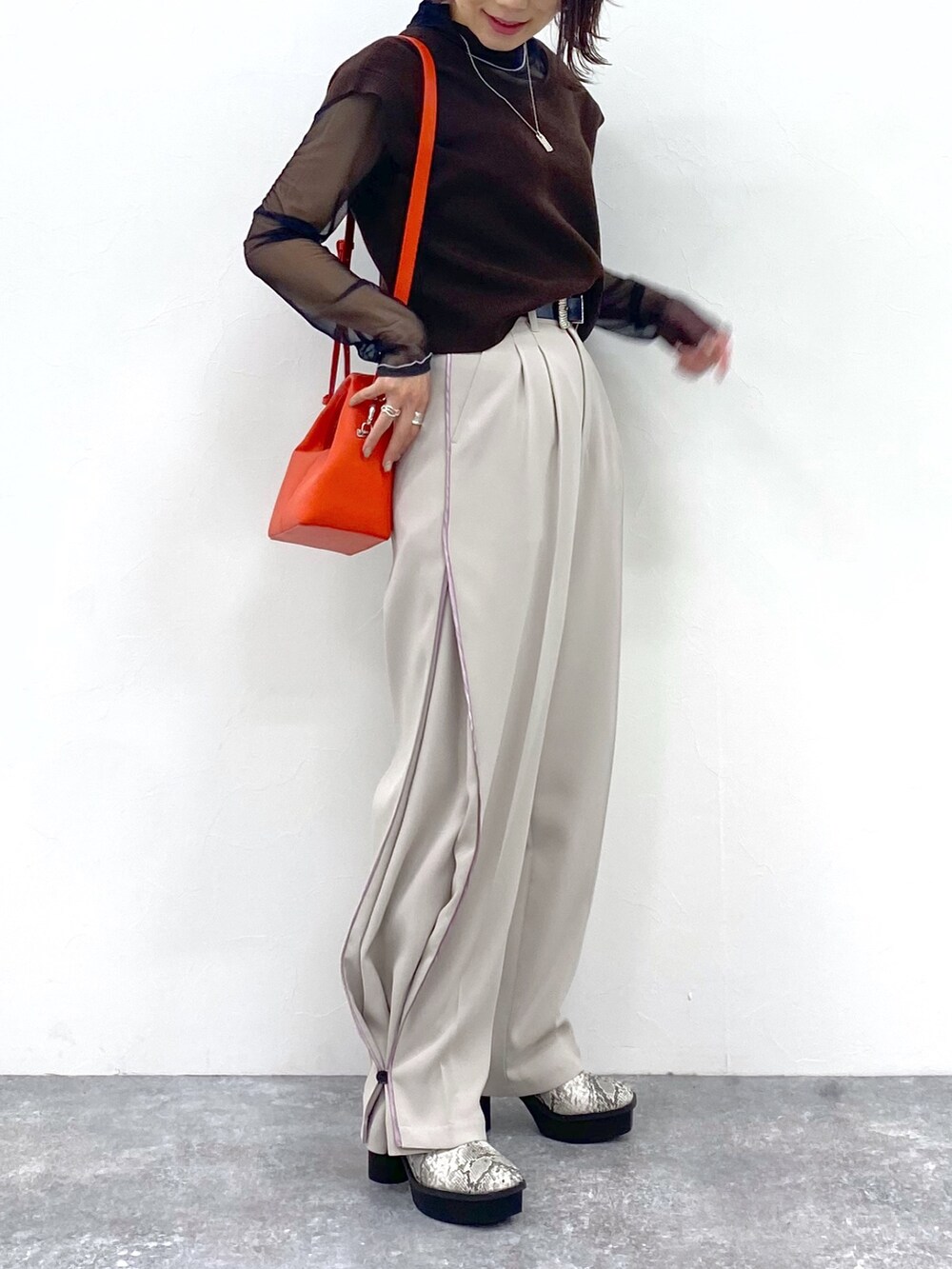 ベージュ系のスラックス、オレンジ系のショルダーバッグ、ブラウン系のワンピースを着用したレディースの夏コーディネートの4枚目の写真