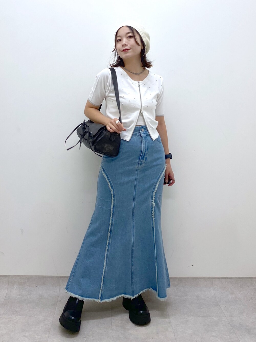 ブルー系のデニムスカート、ホワイト系のニット/セーター、ブラック系のショルダーバッグを着用したレディースの夏コーディネートの4枚目の写真
