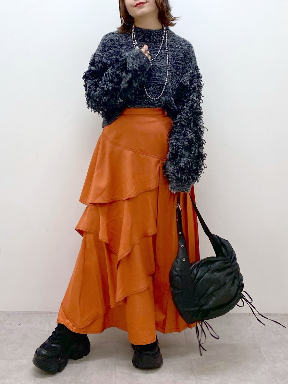ブラック系のニット/セーター、オレンジ系のスカート、ブラック系のショルダーバッグを着用したレディースの冬コーディネートの3枚目の写真