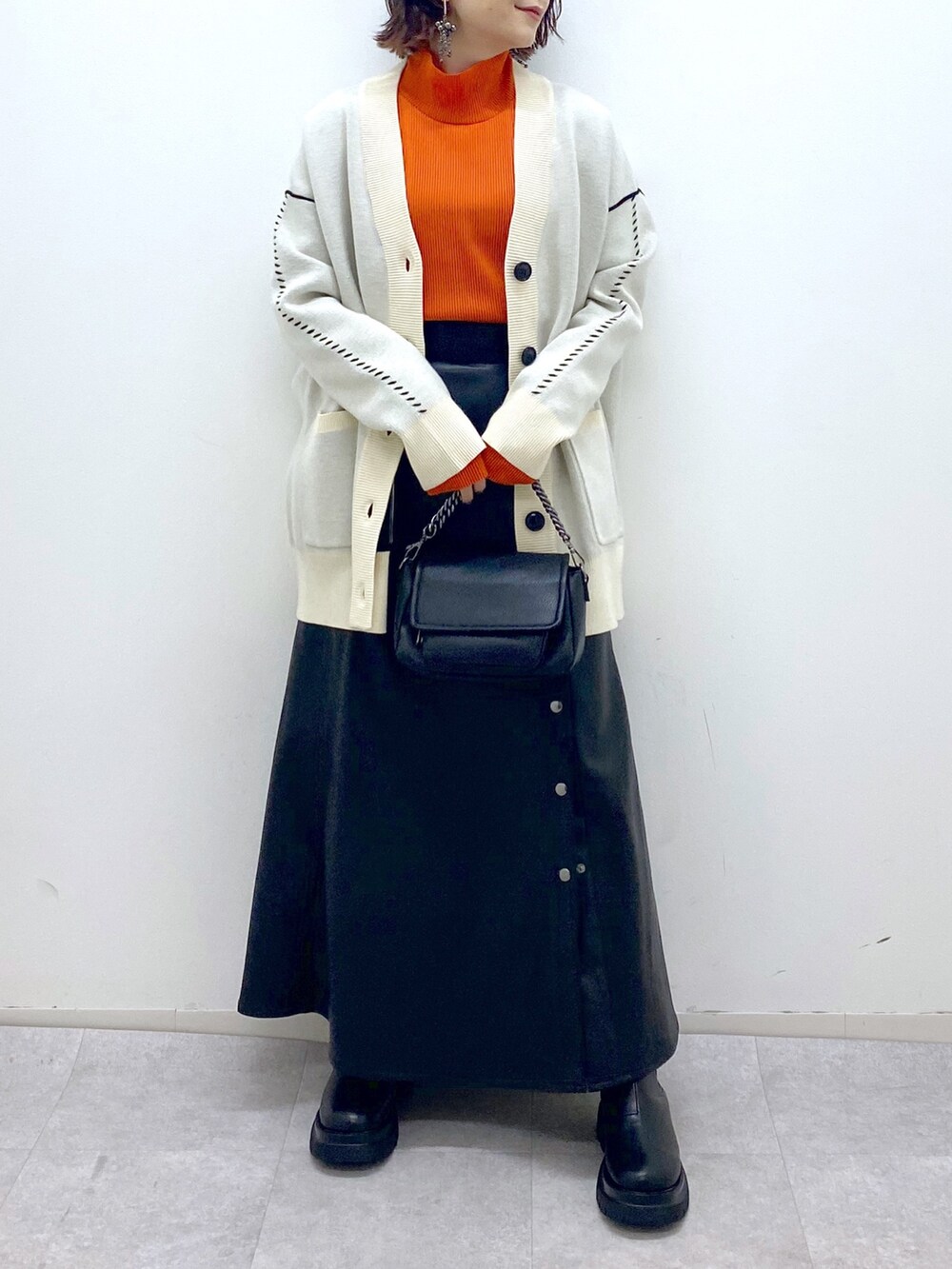 ブラック系のスカート、ブラック系のバッグ、オレンジ系のトップスを着用したレディースの秋コーディネートの5枚目の写真