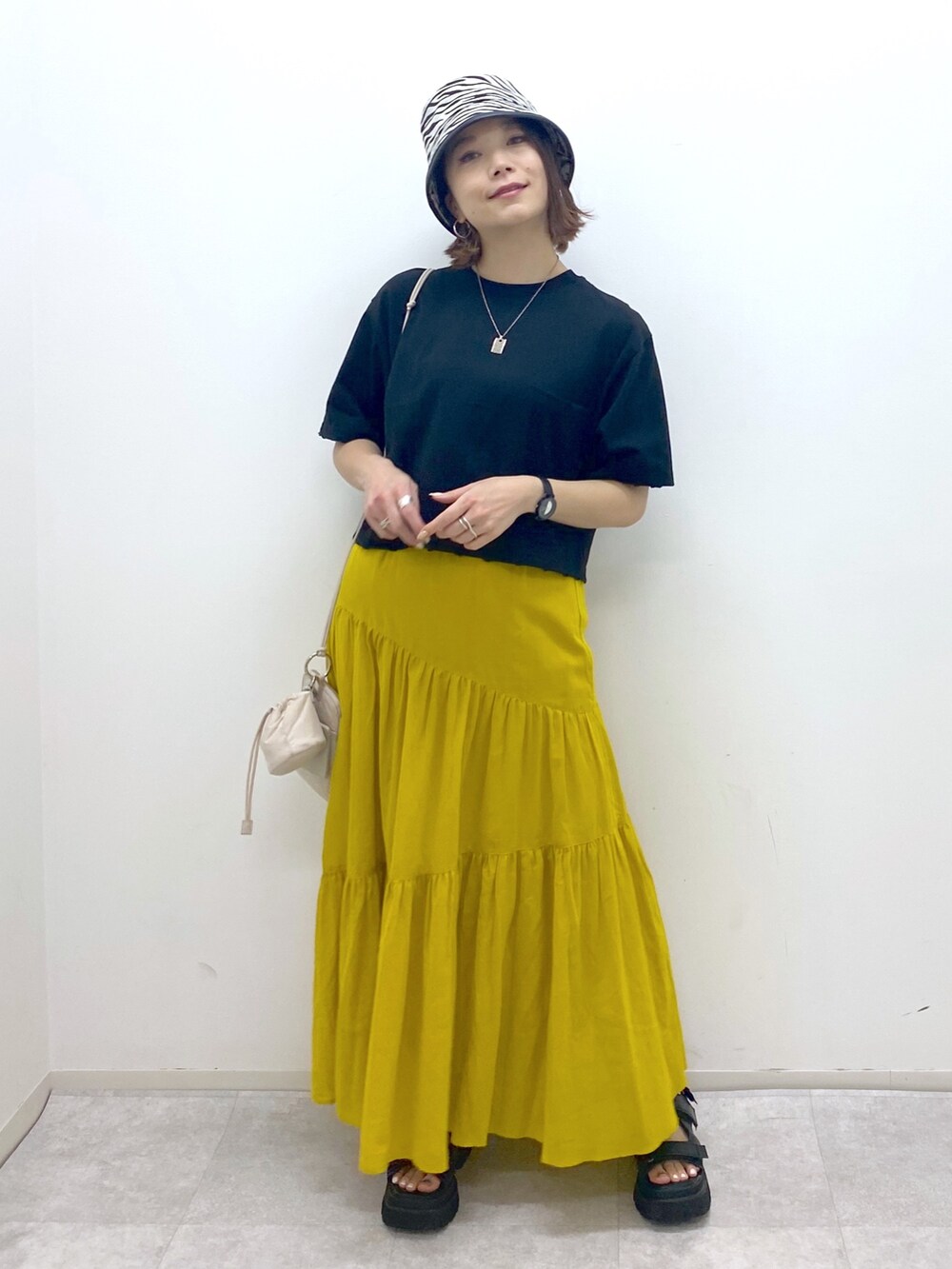 ブラック系のトップス、イエロー系のスカート、ベージュ系のショルダーバッグを着用したレディースの夏コーディネートの2枚目の写真