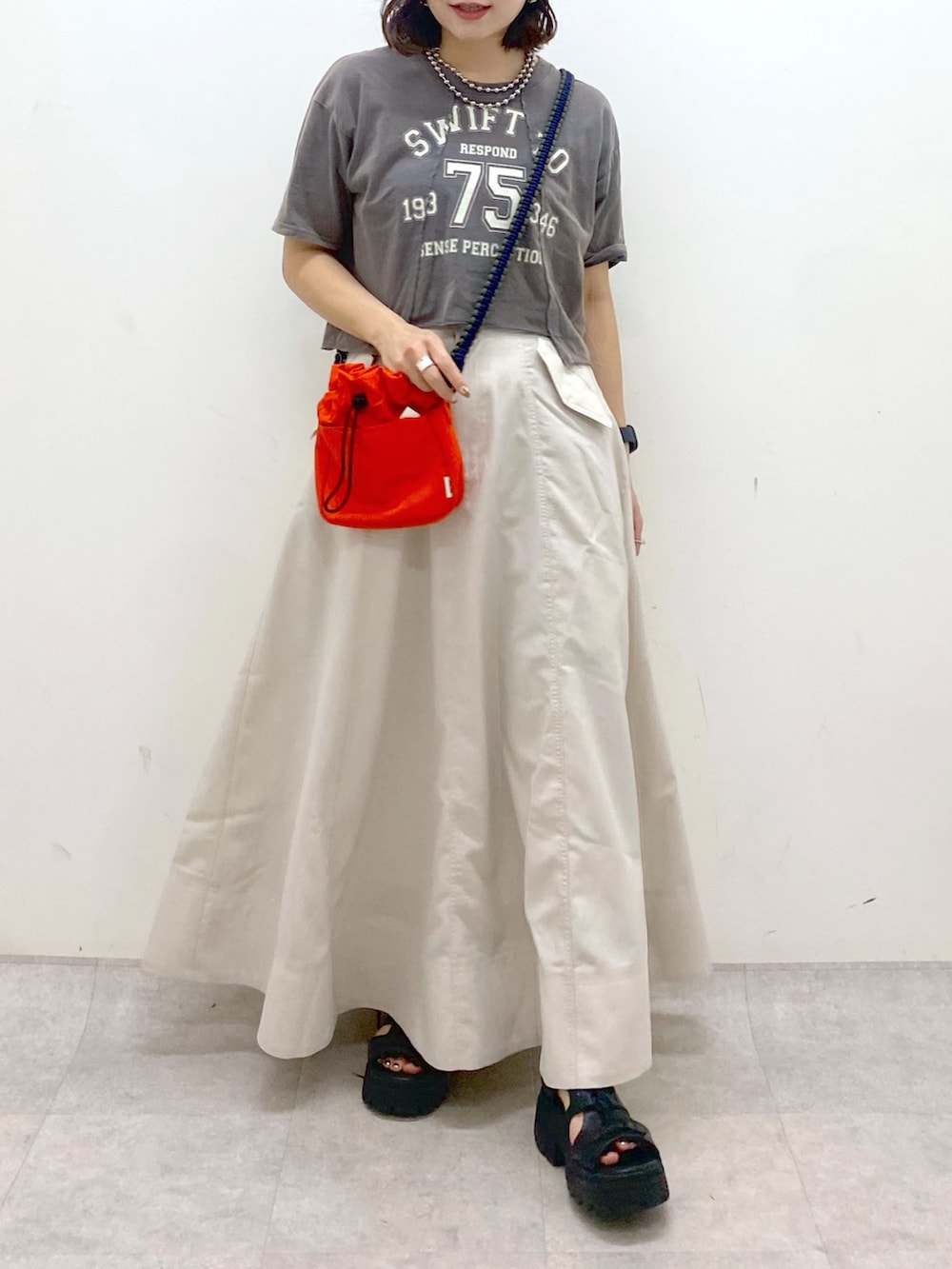 ブラック系のTシャツ/カットソー、オレンジ系のショルダーバッグ、ベージュ系のスカートを着用したレディースの夏コーディネートの3枚目の写真