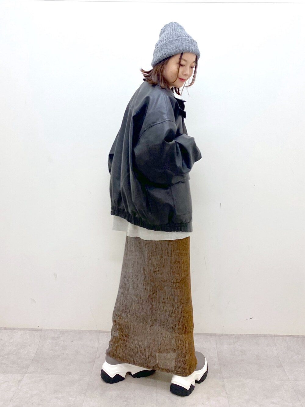 グレー系のニット/セーター、ブラック系のブルゾン、ゴールド系のスカートを着用したレディースの秋コーディネートの5枚目の写真